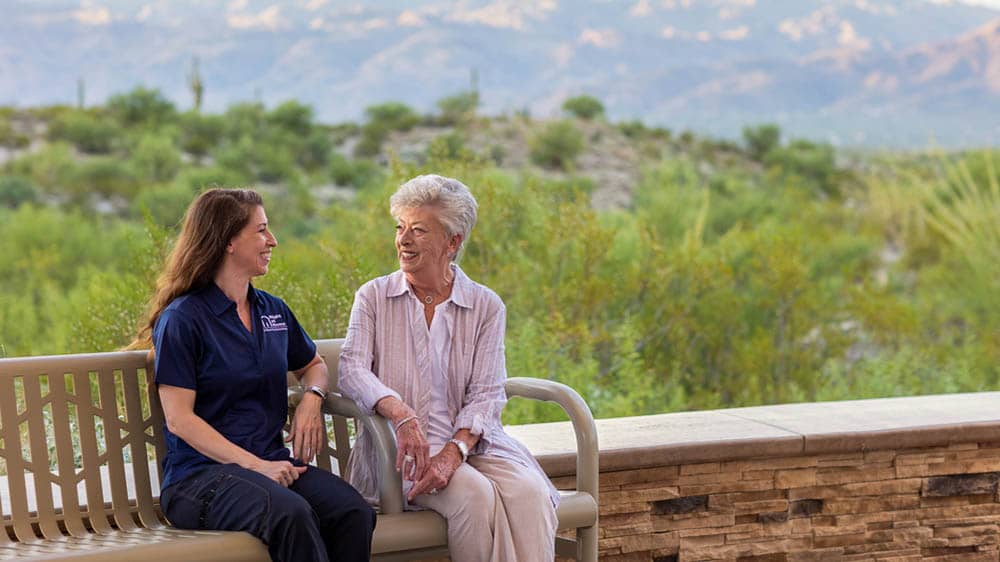 A female Right at Home Caregiver is sitting next to her senior female client on a bench outside