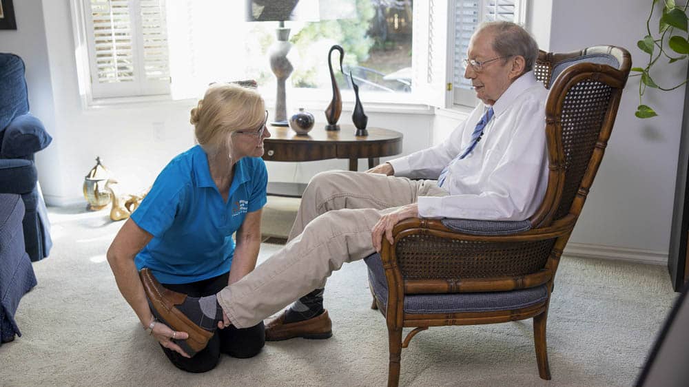 A female caregiver helping a senior male put on shoes