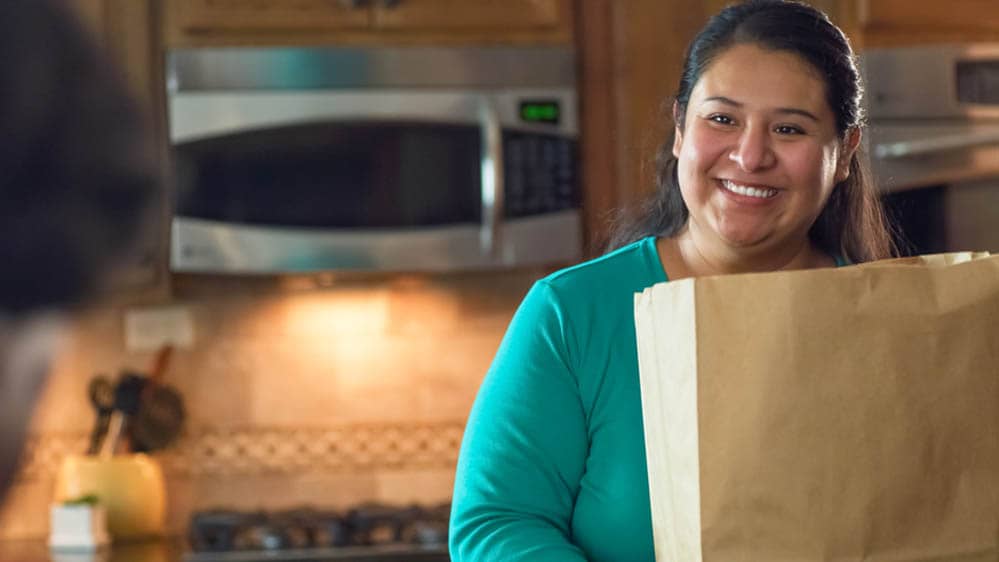 A female Right at Home caregiver setting a grocery bag on a counter in kitchen