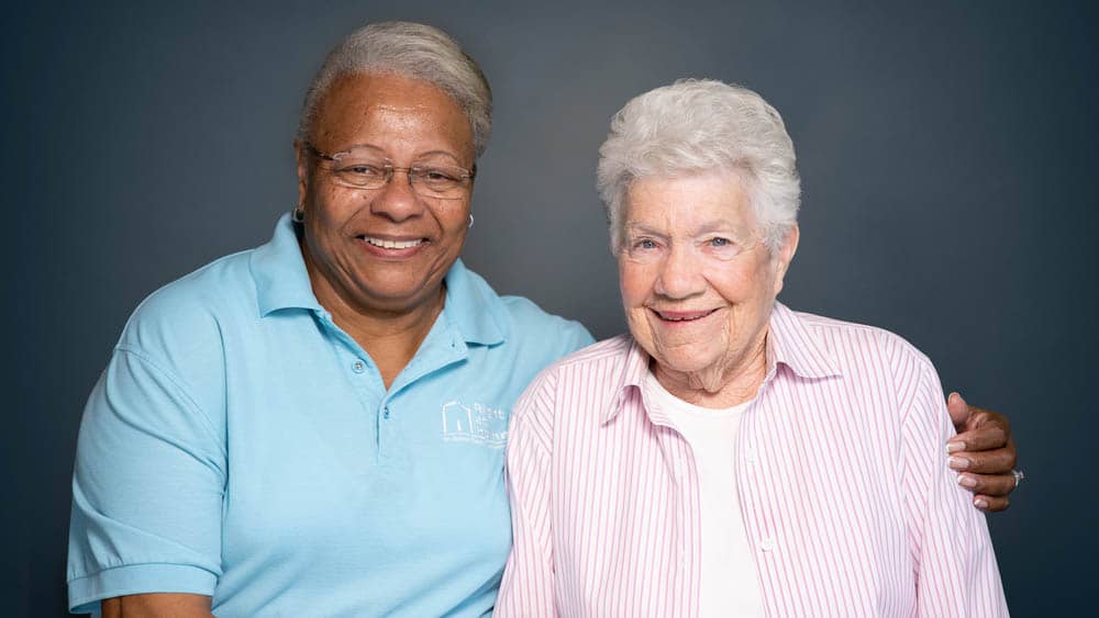 A female Right at Home caregiver sitting with her arm around a senior female client