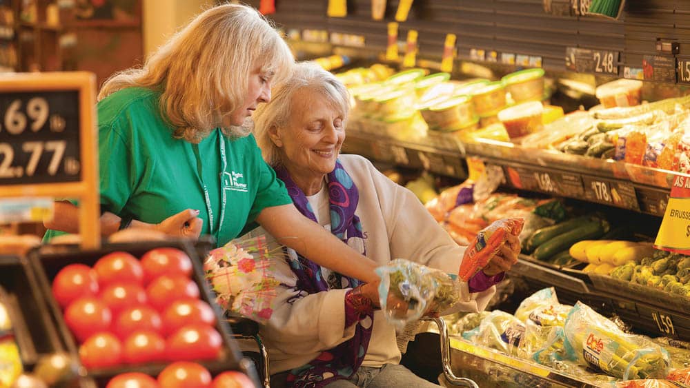 senior female client doing her grocery shopping with the assistance of a female right at home caregiver