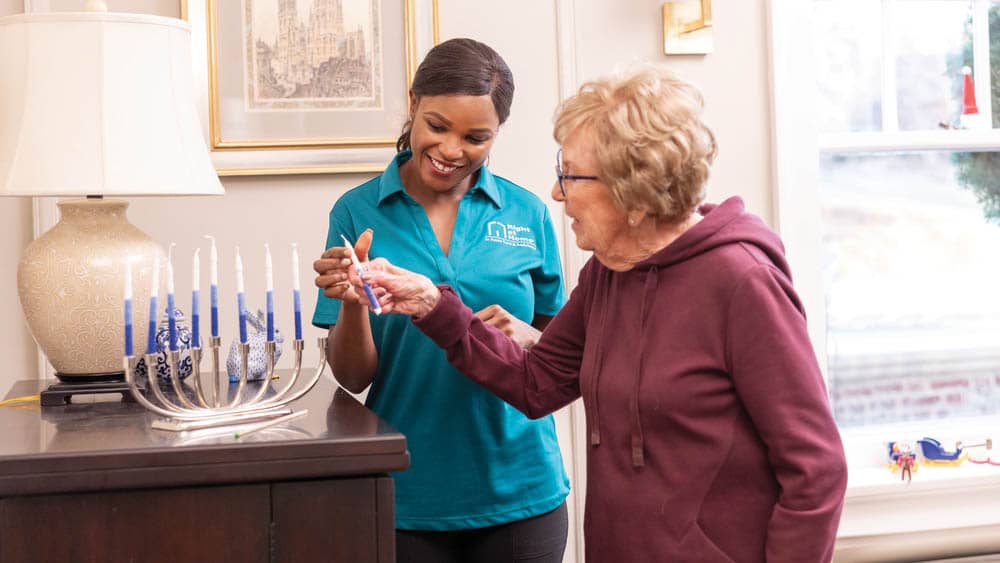 Senior female client lighting a Hanukkah candle with the assistance of her female right at home caregiver