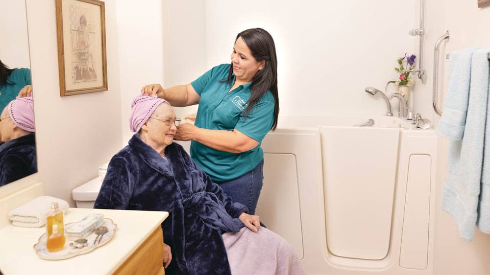 a female Right at Home caregiver is helping a senior female with her hair in the bathroom