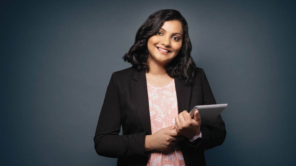 Female smiling holding a notepad in front of gray background