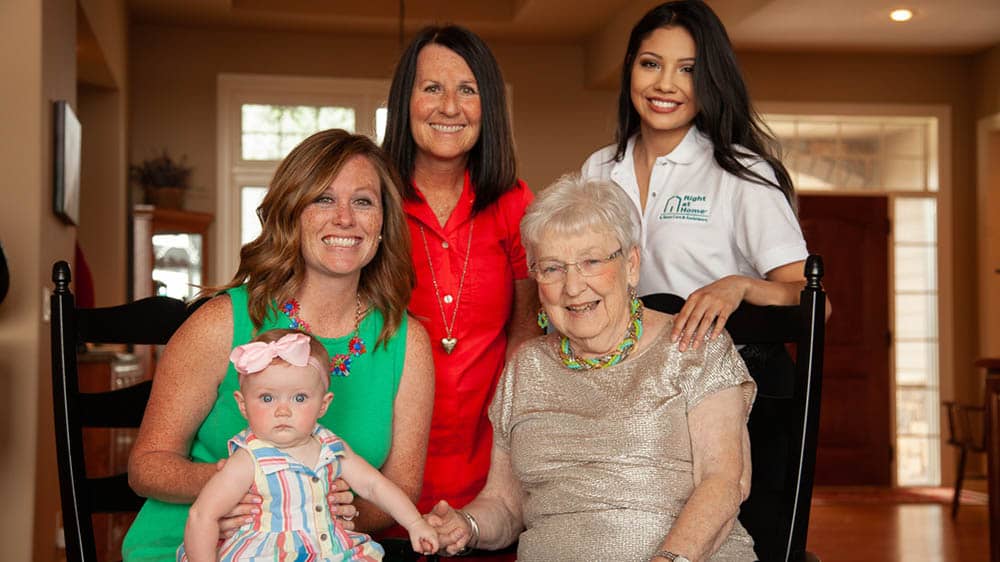 A family photo of four generations of women and a female Right at Home caregiver