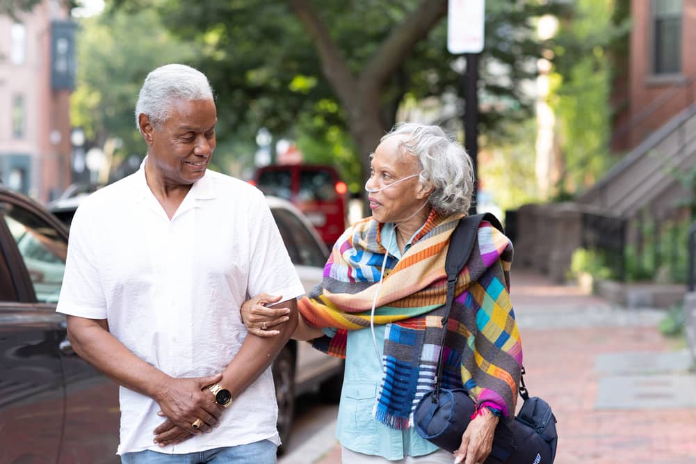 A senior male and senior female are walking arm in arm down the street