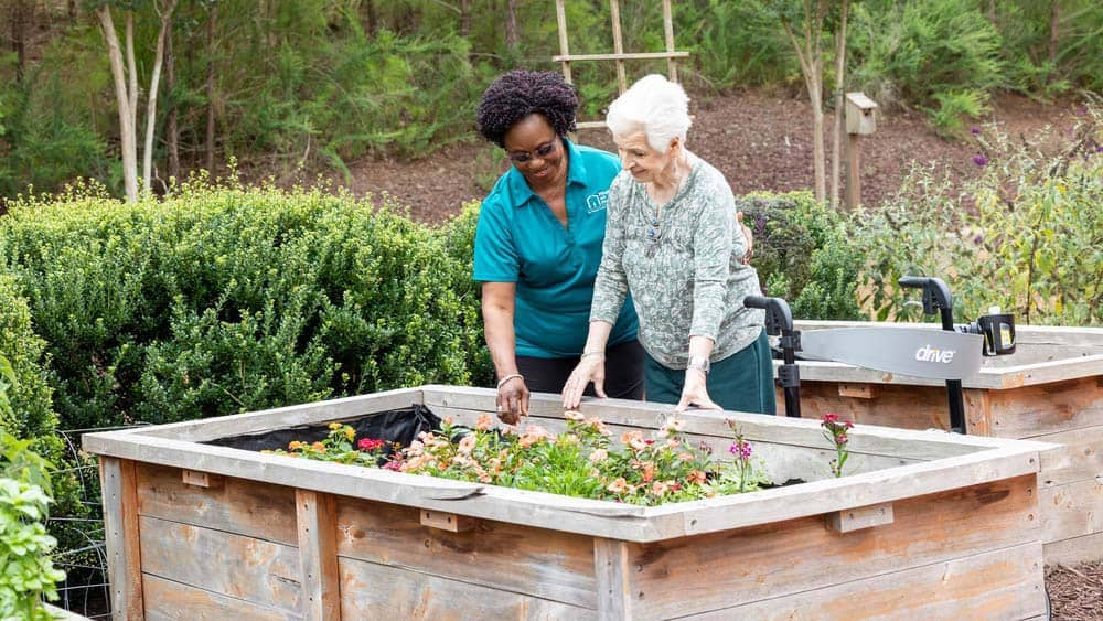 Female Right at Home caregiver helping a senior female client garden in her backyard