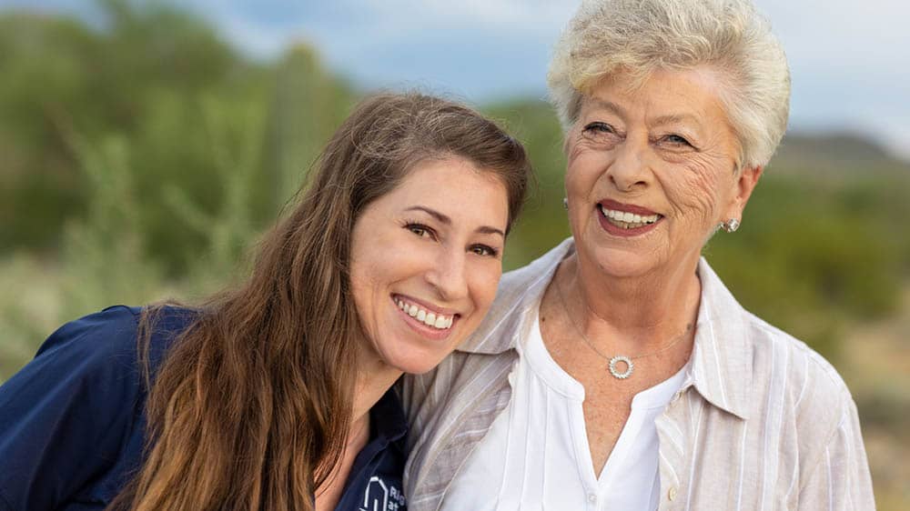 A senior female client standing outside next to her female Right at Home caregiver smiling together