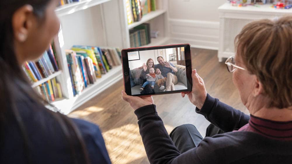 A female Right at Home caregiver looks on as a senior female client is facetime chatting with her family on a tablet