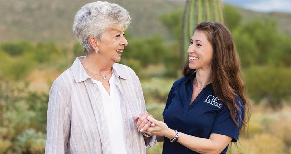 Female Right at Home caregiver holding the hand of a senior female outside, while smiling