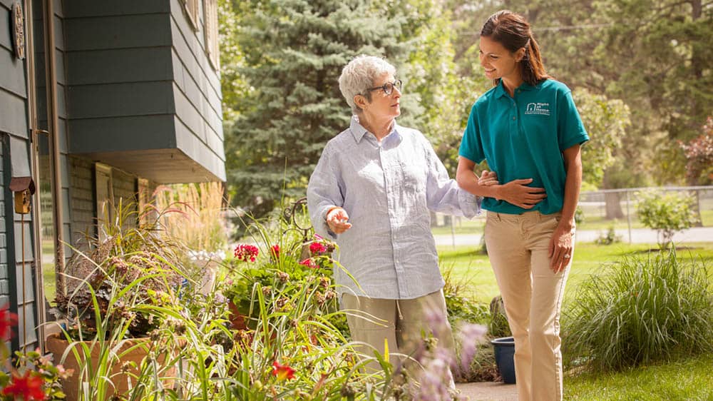 Senior female client and female Right at Home caregiver walking outside arm in arm