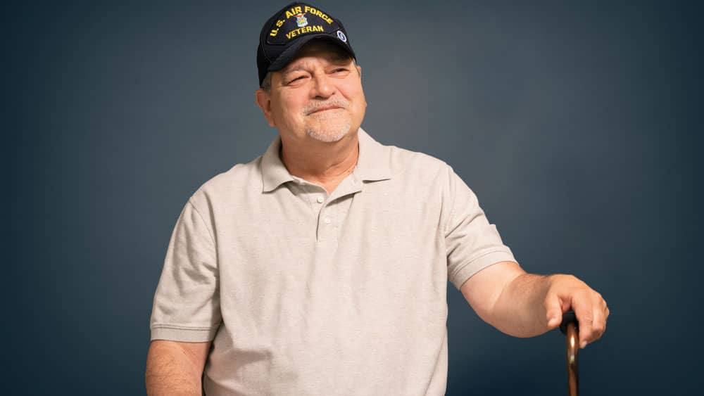 A senior male veteran holding a cane sitting in front of a blue screen