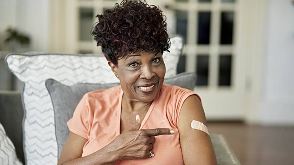 Senior African-American woman pointing to a Band-Aid from a vaccination with a smile.