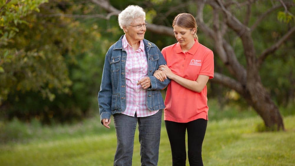 Senior female client walking arm in arm with a female Right at Home caregiver outside