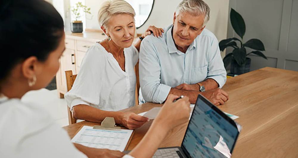 a senior couple sitting at a table with a long term care insurance specialist who is using a laptop