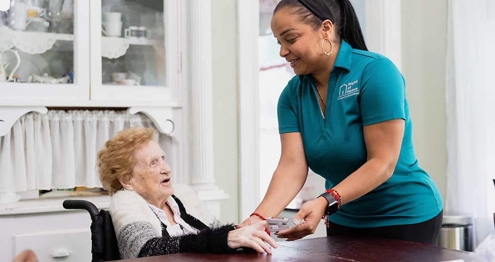 A senior female receives a blood oxygen level test, performed by a female caregiver in the kitchen