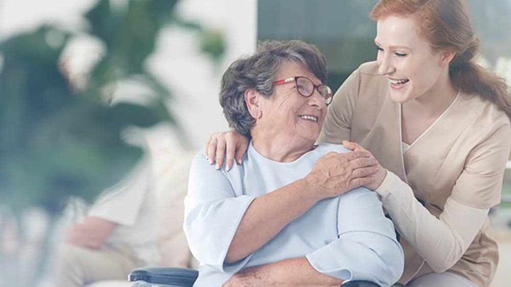 senior female client in a wheelchair smiling with female caregiver