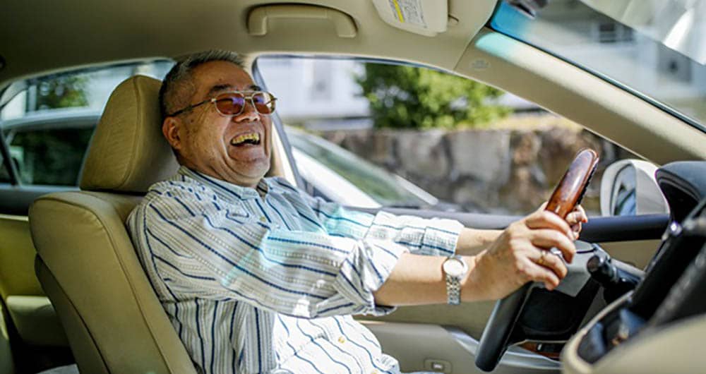 A senior man is driving a car, while smiling