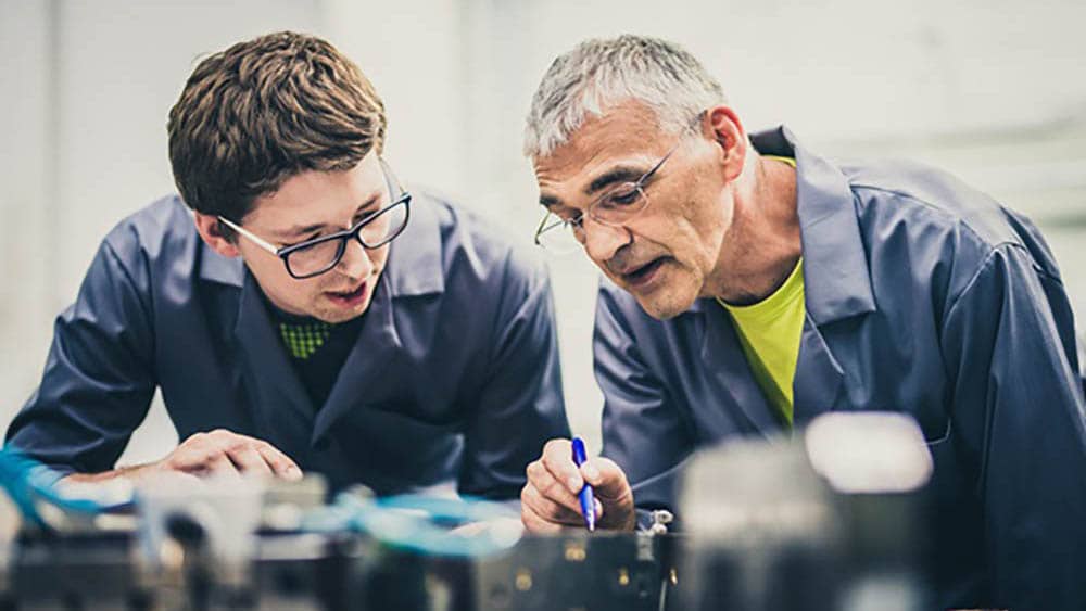 senior man pointing to a piece of technology, showing younger man something