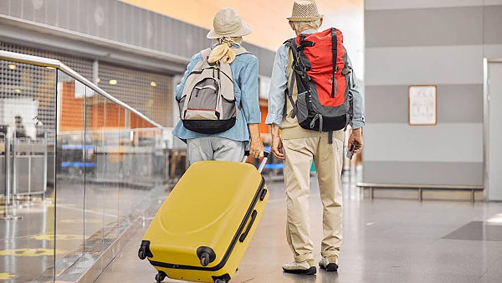 A male and female senior couple in an airport carrying their luggage