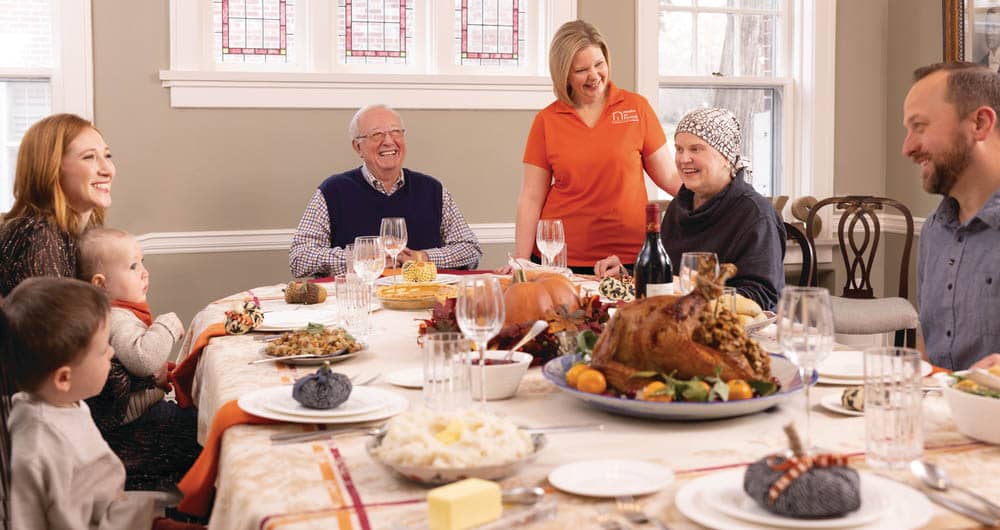 A family sitting down to thanksgiving dinner, with the assistance of a Right at Home caregiver