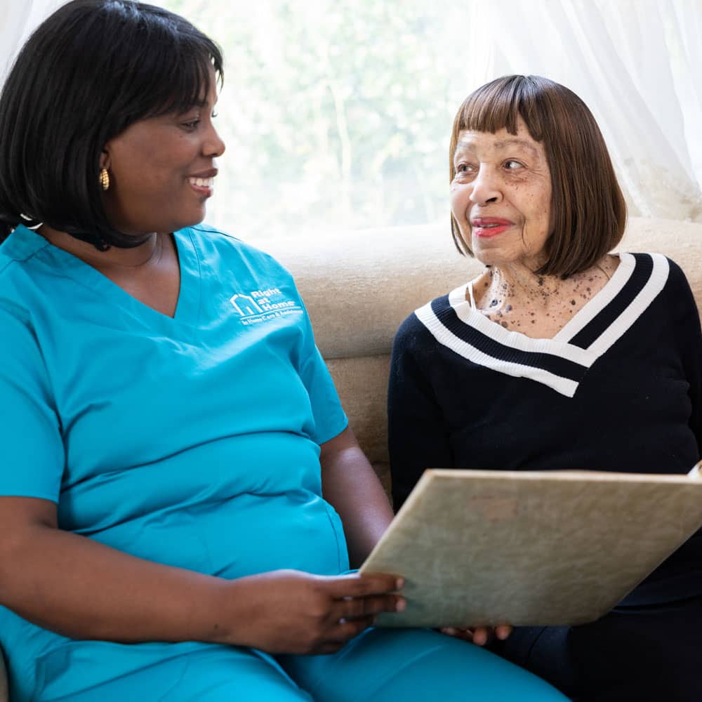 Caregiver and senior sitting on couch looking at photo album