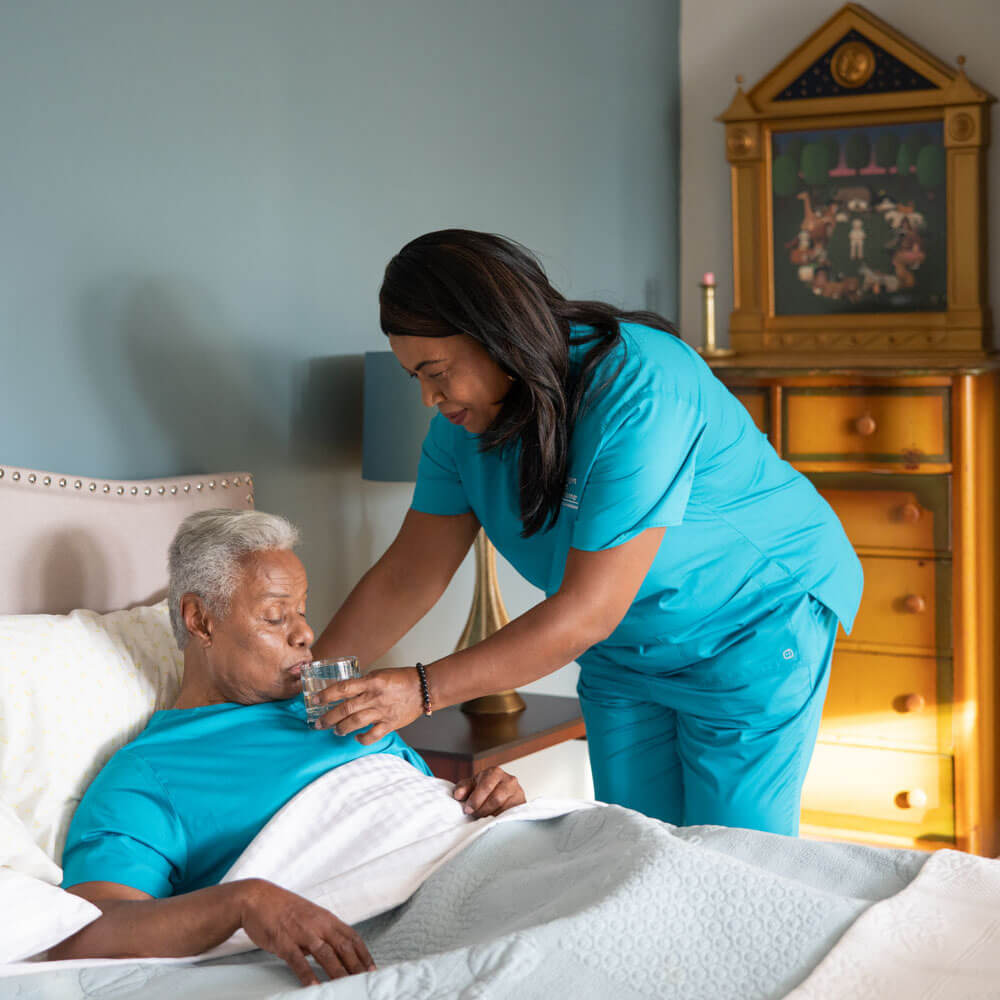 Caregiver giving senior in bed a drink of water