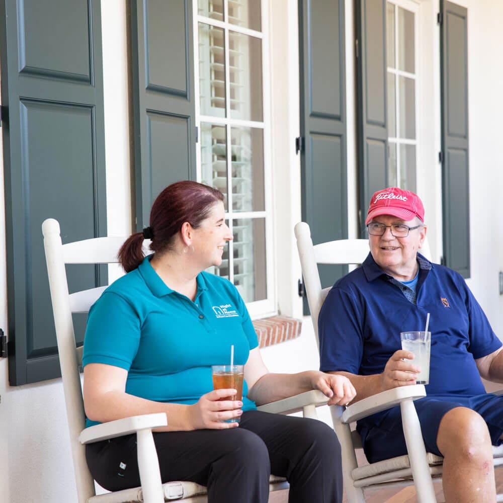 Caregiver and senior sitting in rocking chairs on porch having drinks