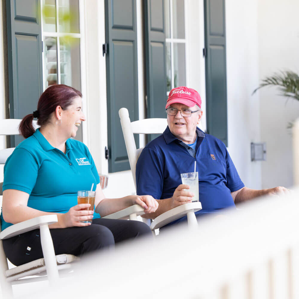 Caregiver and senior sitting in rocking chairs on porch having drinks