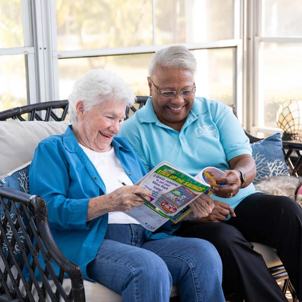 Caregiver and senior sitting in sun room looking at crossword puzzles