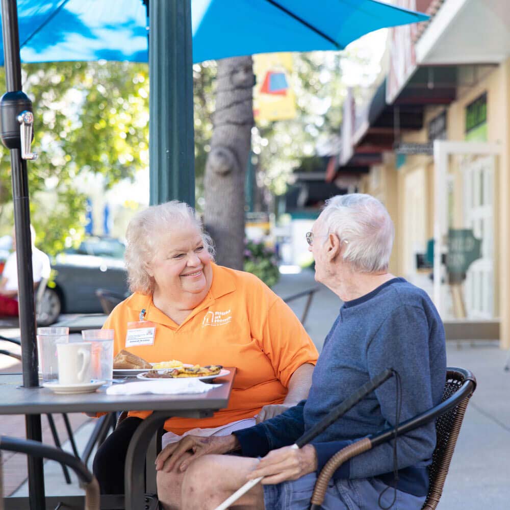 Caregiver and senior having lunch at a an outdoor café under a blue umbrella