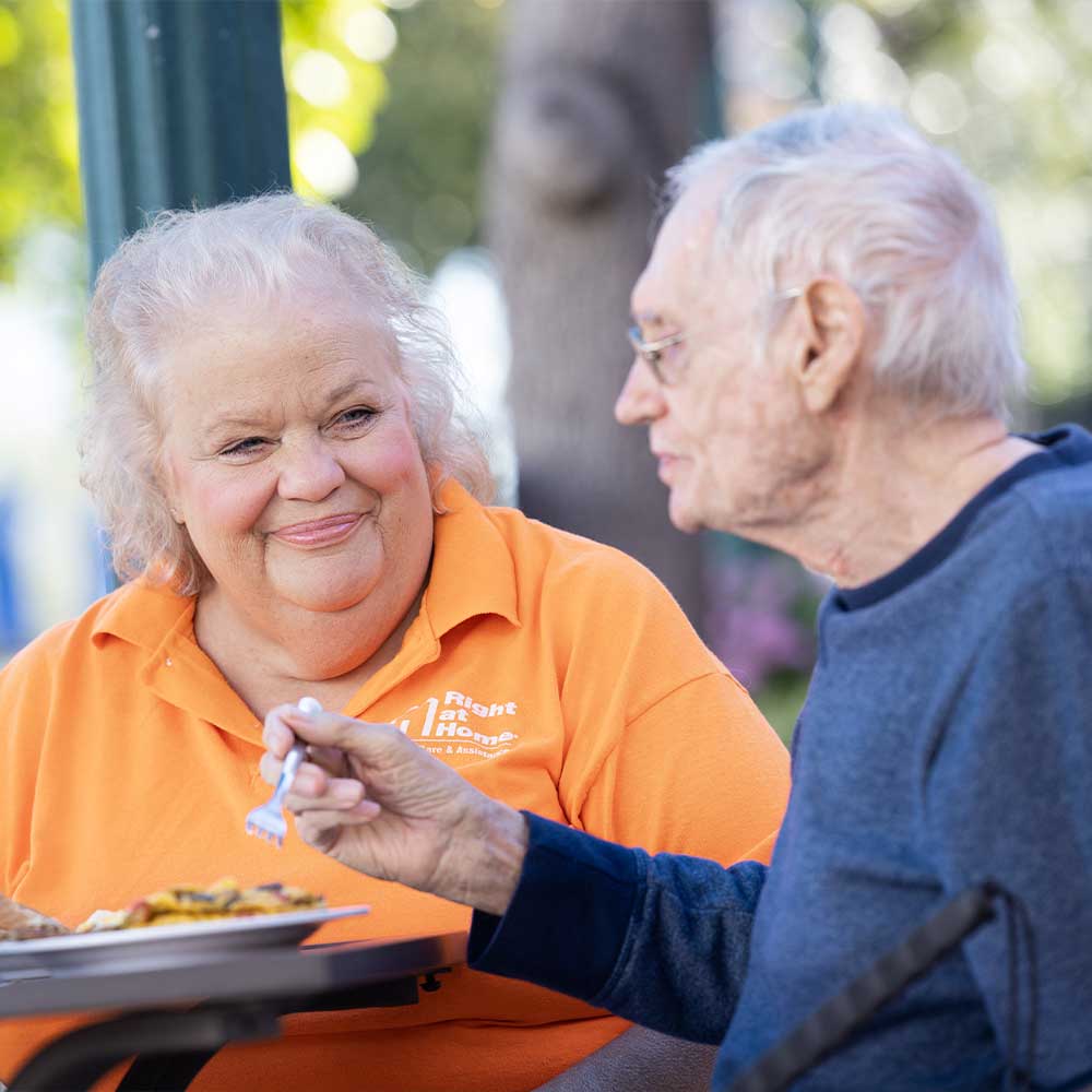 Caregiver and senior having lunch at a an outdoor café under a blue umbrella