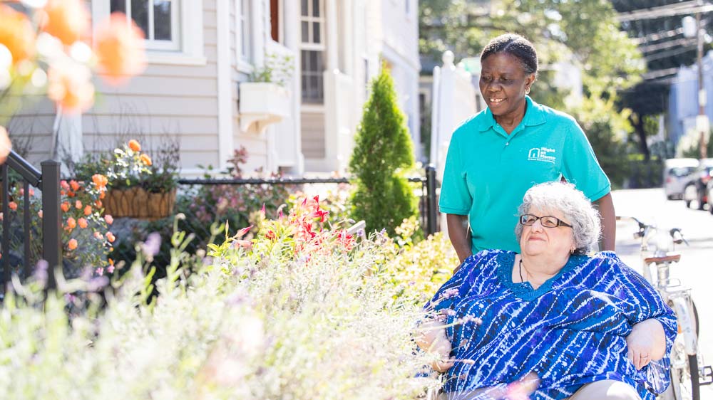 Caregiver pushing client in a wheelchair outdoors.