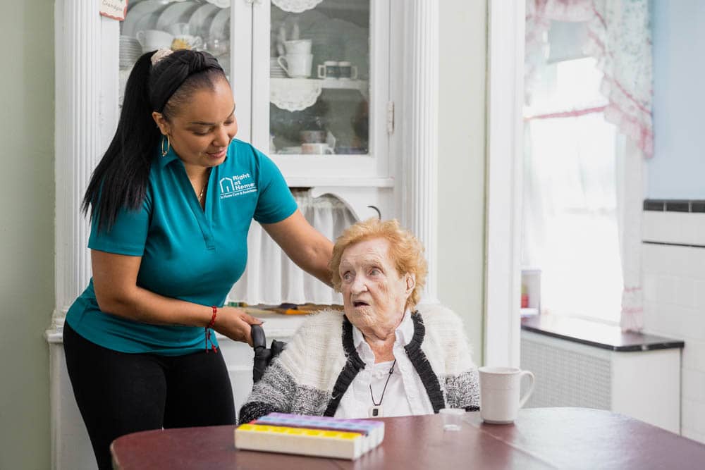 Caregiver pushing client up to the table in her wheelchair.