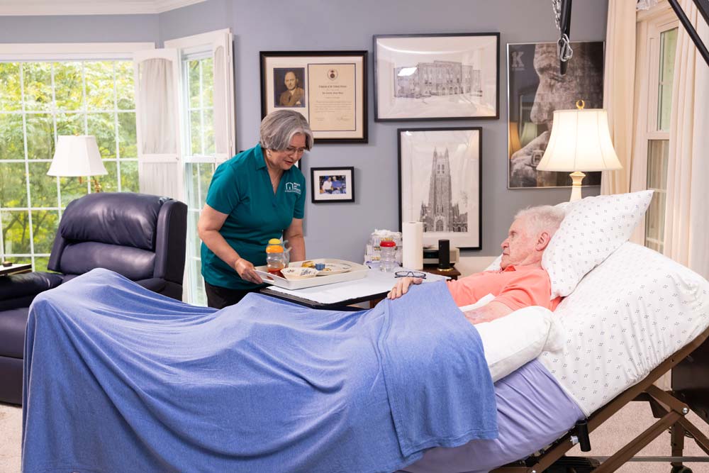 caregiver serving plate of food to senior in bed
