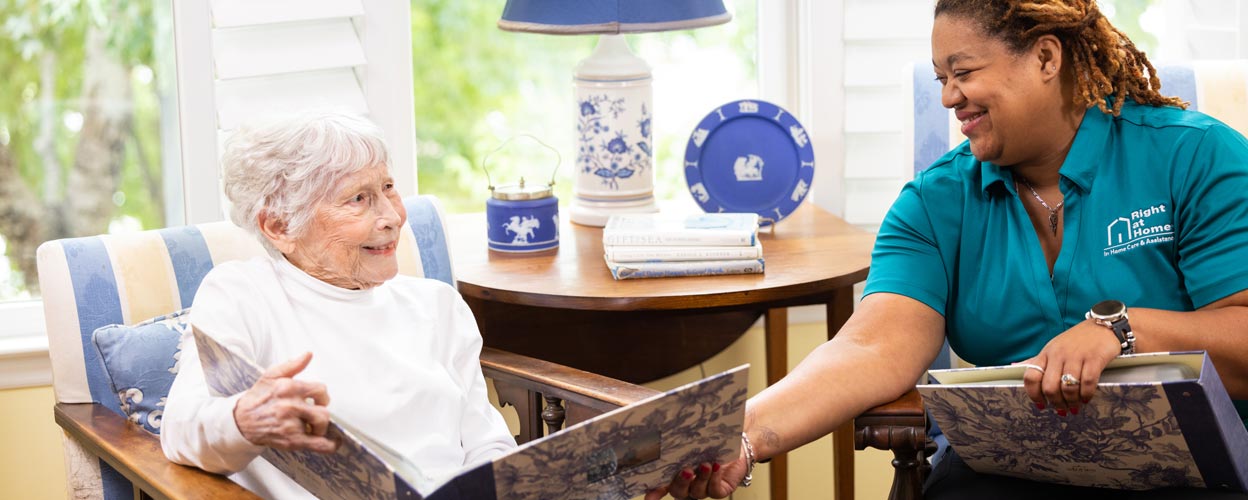 female caregiver and female senior client looking at photo albums while sitting down