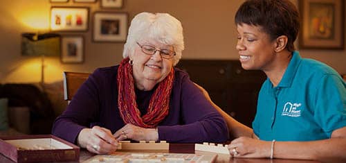 A senior female client and a female Right at Home caregiver are playing scrabble together at a table