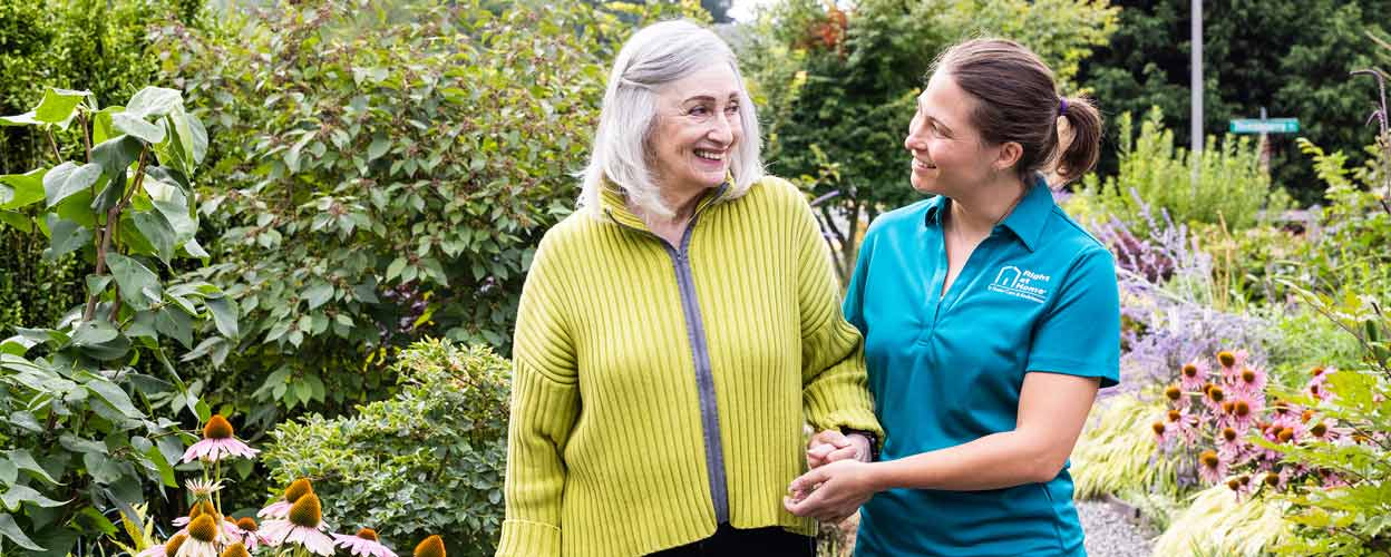 senior woman and female caregiver walking outside on gravel path