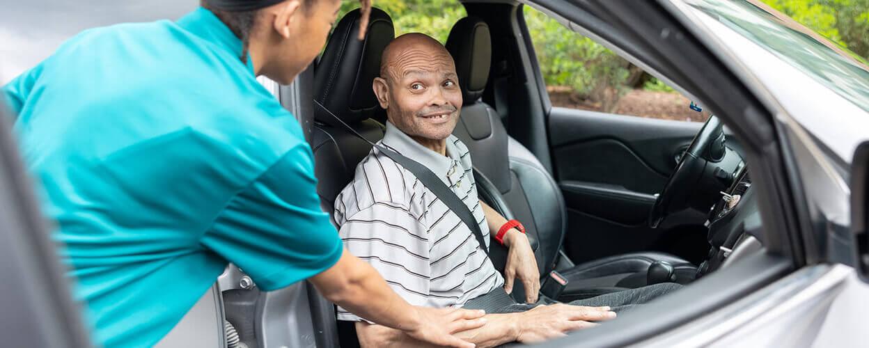 caregiver helping senior male with transportation services