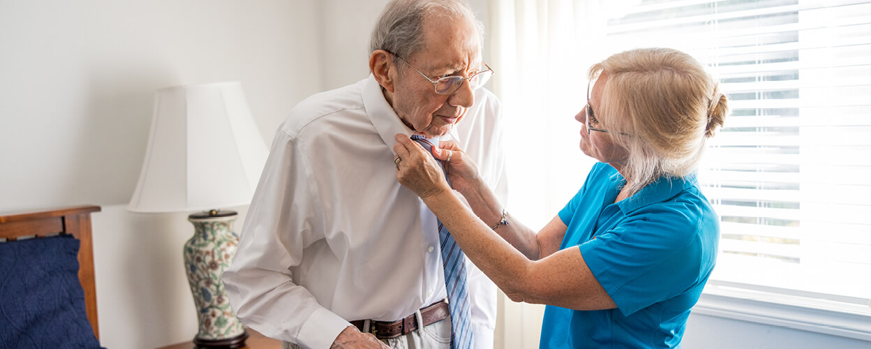 Female caregiver helping client put on his tie. 