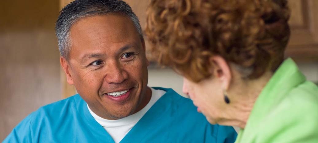 A caregiver in blue smiles at his client.