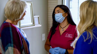 A caregiver in a mask looks at her client while talking to a family member.