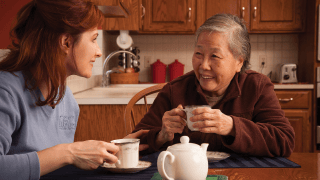 A caregiver smiles at her client over a cup of tea.