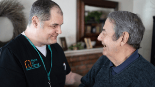 A caregiver smiles at his client, who laughs while telling a story.