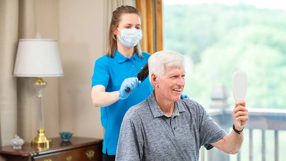 Caregiver with mask brushing hair of senior gentleman