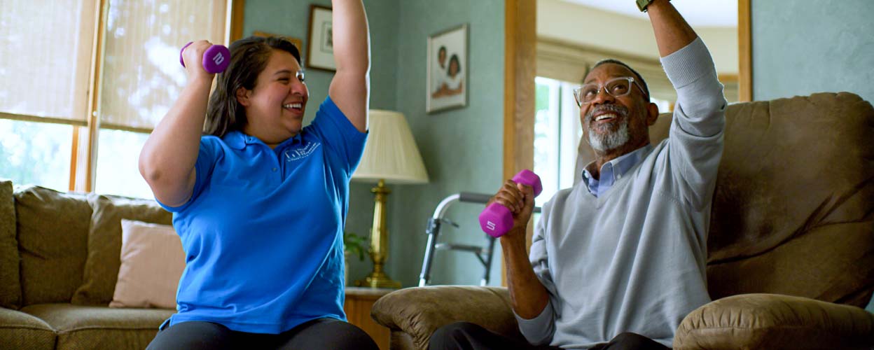 A caregiver shows her patient how to use small hand weights.