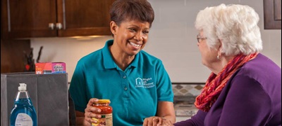 A caregiver talks to her patient, an elderly woman, while they unpack groceries.